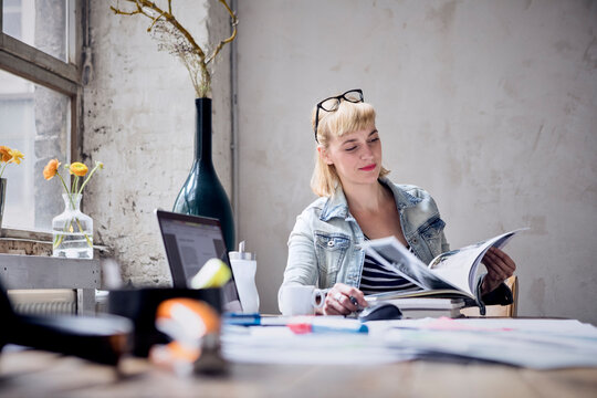 Portrait of smiling woman sitting at desk in a loft leafing through book