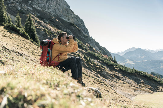 Austria, Tyrol, man having a break during a hiking trip in the mountains looking through binoculars