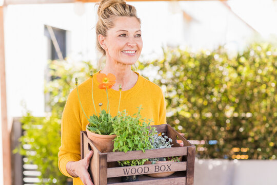 Portrait of happy mature woman with wooden box of plants on terrace