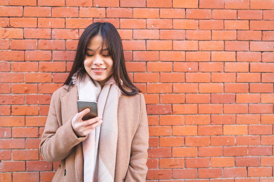 Smiling young woman using cell phone at brick wall