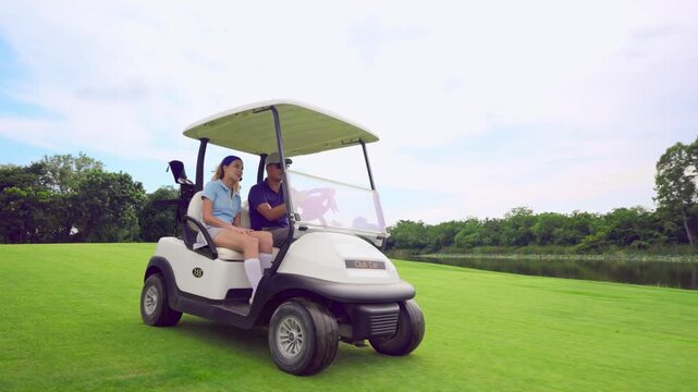 Asian golfer team ride in golf cart together on a scenic golf course. 