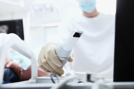 Dentist holds portable 3D scanner in his hand to examine jaw and oral cavity. Creates 3D model of teeth and gums on medical monitor. Dentist performs 3D scan of patient's teeth. Dental health.