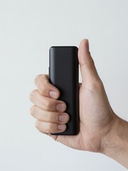 Fototapeta premium Hand Holding a Sleek Black Device Against a Clean White Background for Minimalist Presentation
