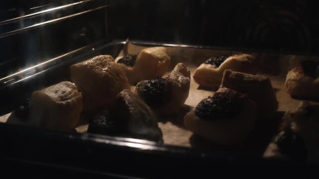 Leaf fat pastry in an oven. Traditional Hungarian lard dessert with plum jam rises behind a dirty oven glass as the dough expands at the very end of the baking process. Grandma&rsquo;s kitchen concept.