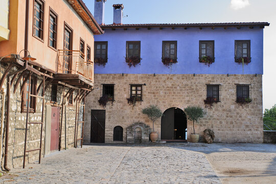 Traditional buildings and stone courtyard in Edessa, Greece. Old stone and painted buildings framing a cobblestone courtyard with olive trees.