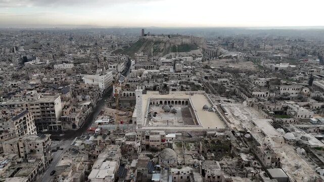 Aerial drone shot over the historic Great Mosque of Aleppo, showcasing the vast courtyard and the ancient Citadel on the horizon in Syria