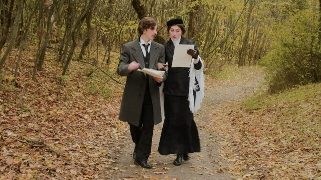 A young man gives a letter to a woman in historical clothing as they walk along an autumn forest path. She reads the document and talks to him while they continue through the peaceful fall landscape.