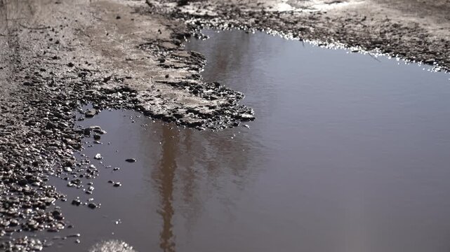 Pothole in asphalt filled with muddy water in spring. Poor road condition, destroyed highway.
