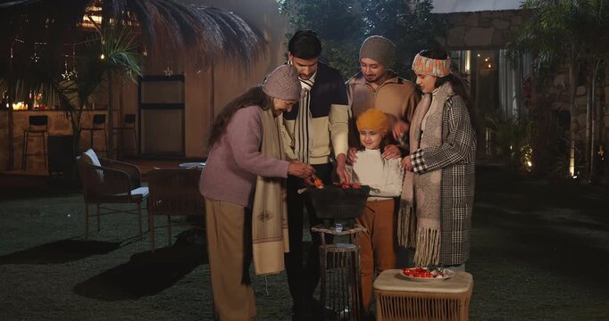 Indian happy mature adult female male speak share gossip enjoy cold winter have fun joy night outdoor garden place mom girl child kid talk with young man cook party food on barbecue spend quality time