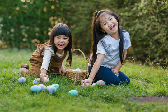 two happy child girl playing together and hunting for Easter eggs into basket on green grass in garden