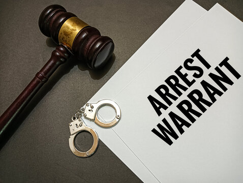 Arrest warrant document with judge gavel and handcuffs on desk representing legal authority, criminal justice system, police enforcement, investigation, and law order concept.