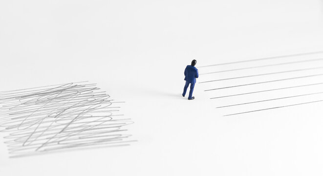Conceptual image showing contrast between chaos and order with a miniature businessman standing between tangled scribble and straight organized lines on white background