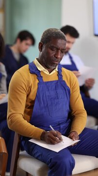 In lecture, African man employee writes on large piece of paper, fills out questionnaire, answers exam questions. Professional aptitude, identification of initiative and talented employees