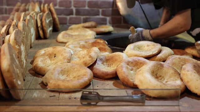 Man baker removing fresh naan flatbread from traditional tandoor oven using a metal hook.