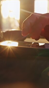 Vertical video. Time Lapse Close Up Of Human Hand Scrolling News Feed And Social Media On Smartphone Beside Keyboard While Warm Sunset Light Fades Through Window Creating Evening Digital Routine And S