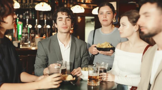 Group of excited young friends fans cheering for sports team together, watching match on TV in big beer bar
