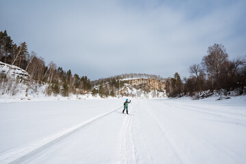Frozen Landscape With Lone Skier. Solitary Skier In Bright Jacket Explores Expansive Icy Wilderness. Lone Individual In Vibrant Green Navigates Broad Frozen Terrain Under Pale Sky