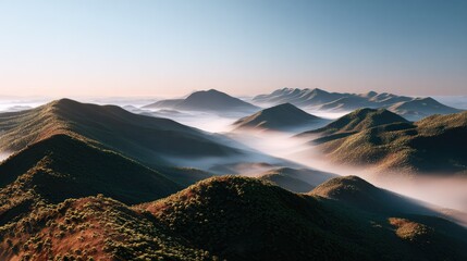 Obraz premium Rolling Mountain Vista: A breathtaking panoramic view of a range of rolling mountains, veiled in a mystical mist under a clear, pale blue sky, evokes a sense of serenity and vastness.
