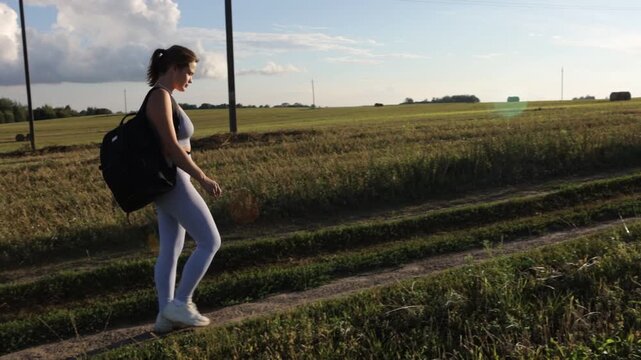 A woman in sportswear walks through a field in a village on a sunny summer day