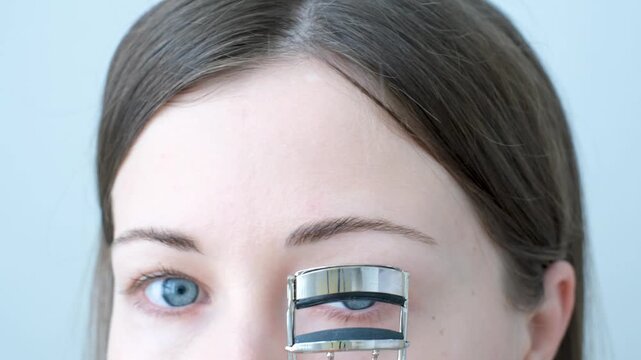Young woman using eyelash curler on gray background close-up.