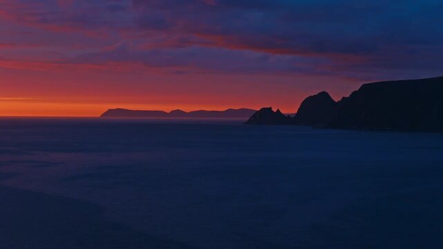 Sandland, Loppa Municipality, Finnmark, Norway - A Vivid Sunset Glows Above the Dark Coastal Cliffs and Calm Sea - Aerial Drone Shot