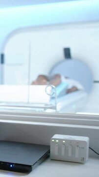 Vertical video: Pointing tech in scrubs at scans on screen in control room as patient entering bore