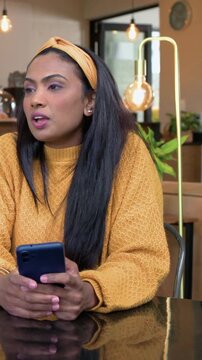 Vertical video: Answering friend, woman in mustard sweater with phone at cafe, barista working