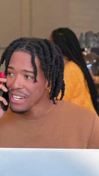 Vertical video: Lifting man in brown knit answering incoming call in cafe, holding phone and laptop