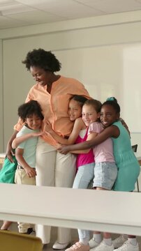 Vertical video: Moving in, kids hugging teacher in peach blouse showing care at school whiteboard
