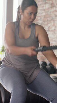 Vertical video: Gripping battle rope, woman powering waves for fitness in gym, wearing grey tank