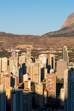 Vertical view of the Benidorm Spain skyline shows urban city architecture and tall skyscrapers near a mountain at sunset with warm evening glow