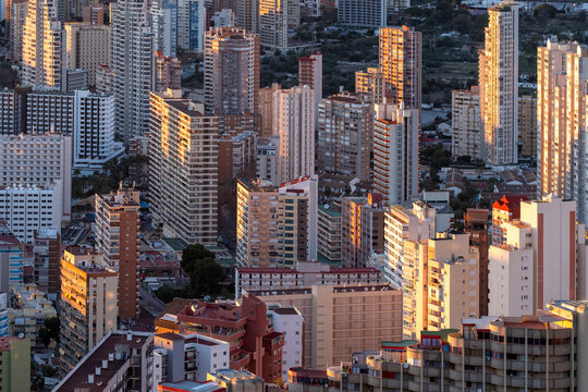 Dense city rooftops lead into the Benidorm Spain skyline where sunlit skyscrapers and urban architecture rise in strong daylight above modern buildings