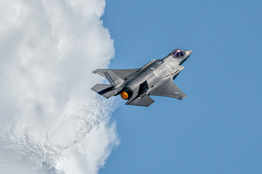 Aerial view of a F35 fighter jet soaring past a cloud, leaving a trail of fire against the clear blue sky, Singapore Air Show 2026, Singapore.