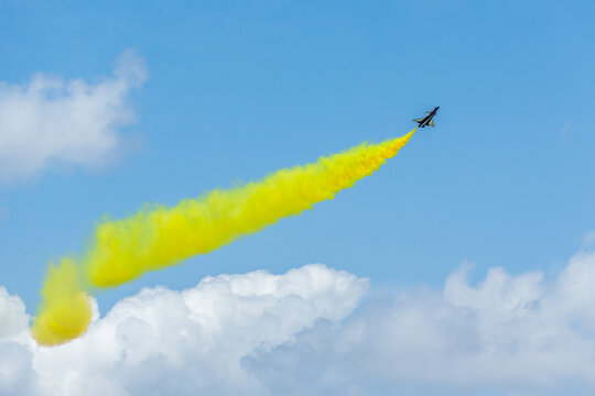Aerial view of a fighter jet soaring through the sky, leaving a trail of vibrant yellow smoke against the backdrop of fluffy white clouds, Changi Exhibition Centre, Singapore Air Show 2026, Singapore.