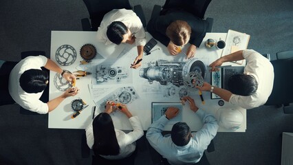 Fototapeta premium Top view of engineer pointing at turbine engine at meeting table with equipment. Aerial view of professional project manager talking and discussing about electronic generator system. Alimentation.