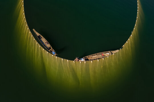 Aerial view of fishing boats casting nets, their golden hues contrasting with the dark waters, creating a mesmerizing circular pattern, Kolkata, West Bengal, India.
