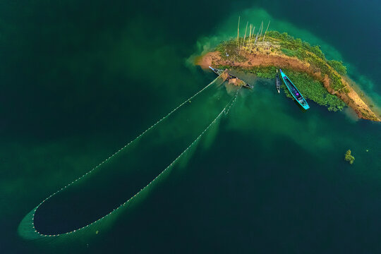 Aerial view of a lush island surrounded by deep turquoise water, with fishing nets cast wide, a serene scene of nature's bounty, Kolkata, West Bengal, India.