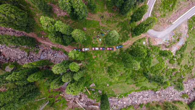 Aerial view of cars parked neatly in a row amidst vibrant green trees and grass along a rugged path, Pathiali, Azad Kashmir, Pakistan.