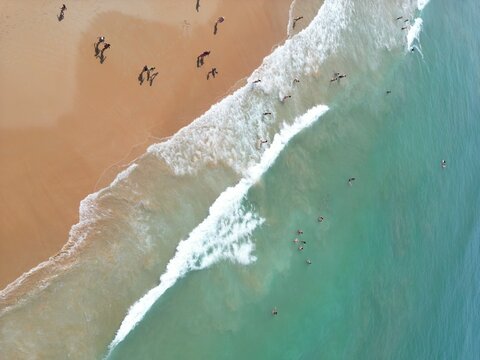 Aerial view of golden sands meeting the turquoise waters, where tiny figures dot the shoreline and waves crash in white foam, Barbate, Andalusia, Spain.