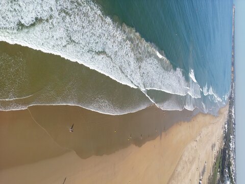 Aerial view of golden sands meeting the turquoise sea in a dance of white-crested waves, Barbate, Andalusia, Spain.