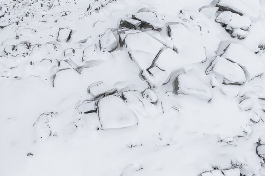 Aerial view of a snow-covered landscape, where jagged rocks are dusted with white, creating a stark contrast between light and shadow, Senjahopen, Troms, Norway.