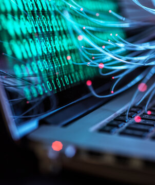 Binary code and fibre optic representing computer virus attack on laptop