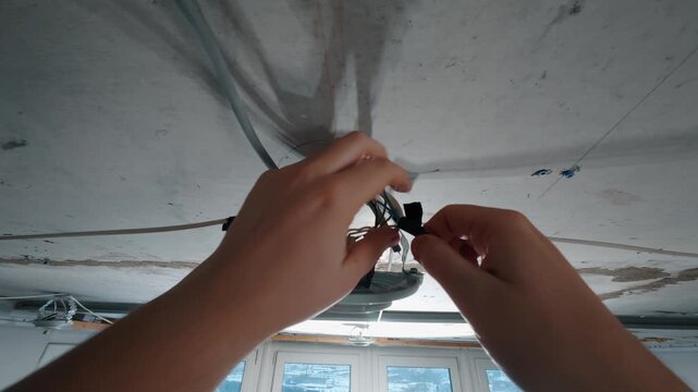 Hands installing ceiling light fixture with electrical wires