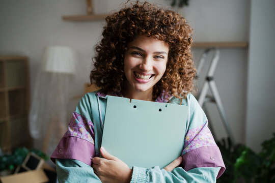 Smiling woman with curly hair holding clipboard indoors in casual home setting