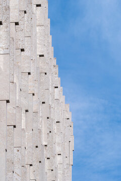 Vertical concrete building facade with abstract geometry and pronounced texture rising into blue sky creating minimal architecture background