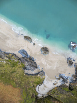 Aerial view of turquoise waters meeting the sandy beach, with rugged cliffs adding a dramatic contrast to the scene, Fowey, Cornwall, United Kingdom.