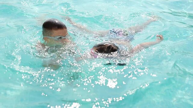 Children with goggles playing in a swimming pool, showing various stages of submersion.