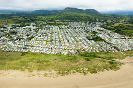 Aerial view of rows of tightly packed mobile homes against the backdrop of distant mountains and a sandy beach, Porthmadog, Wales, United Kingdom.