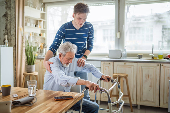 Young man helping senior father using walker at home
