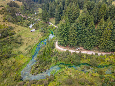 Aerial view of a winding stream cuts through verdant meadows, framed by dense forests and a solitary building, Tapapa, Waikato Region, New Zealand.